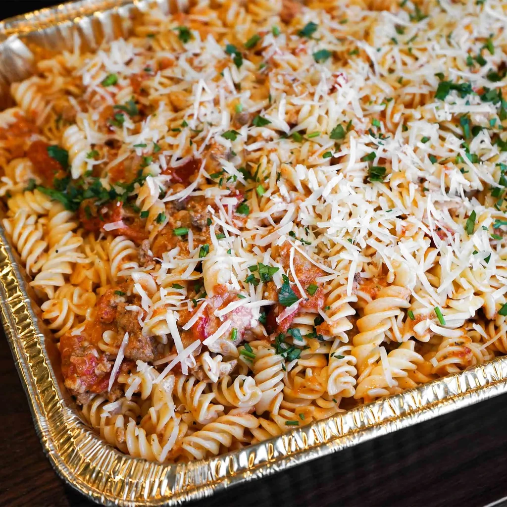 Fusilli pasta with meat sauce, cheese, and herbs in a catering tray.