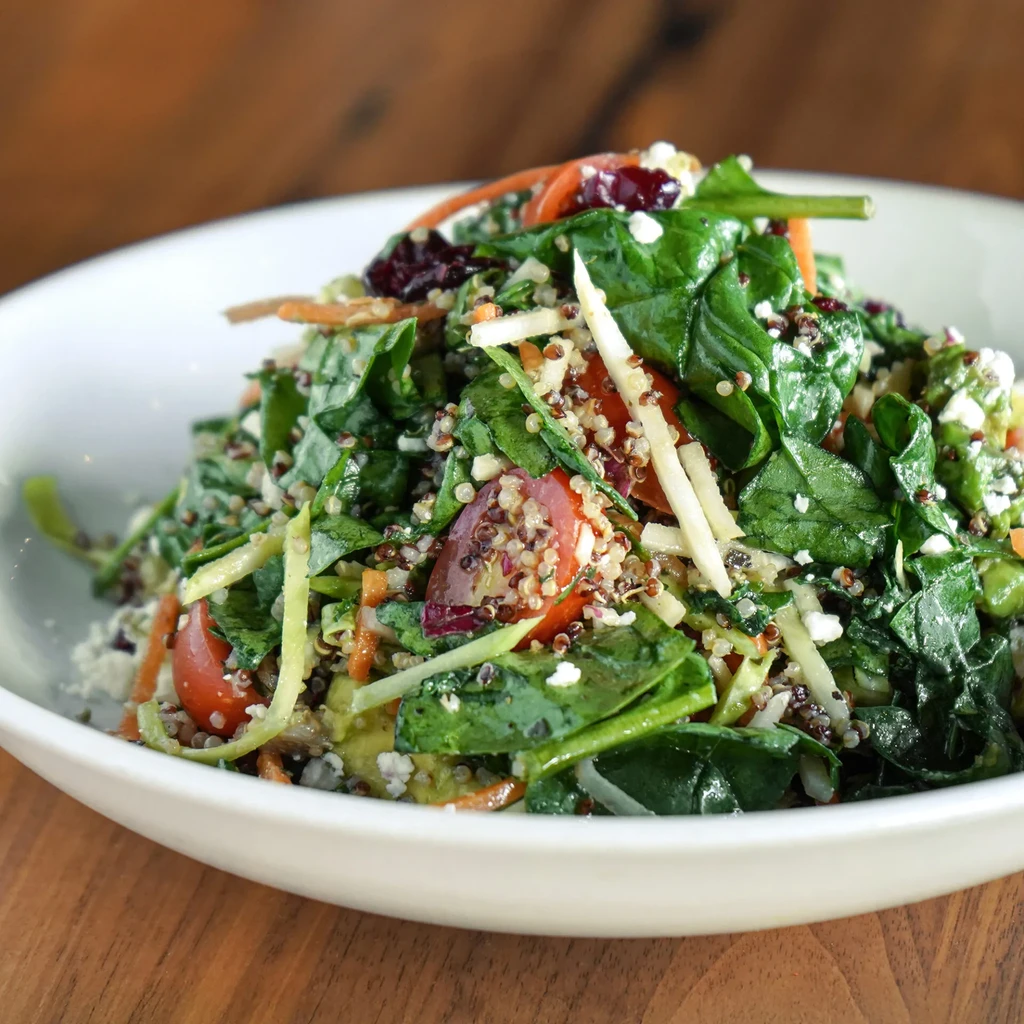 Vibrant salad with spinach, quinoa, tomatoes, carrots, and crumbled feta.