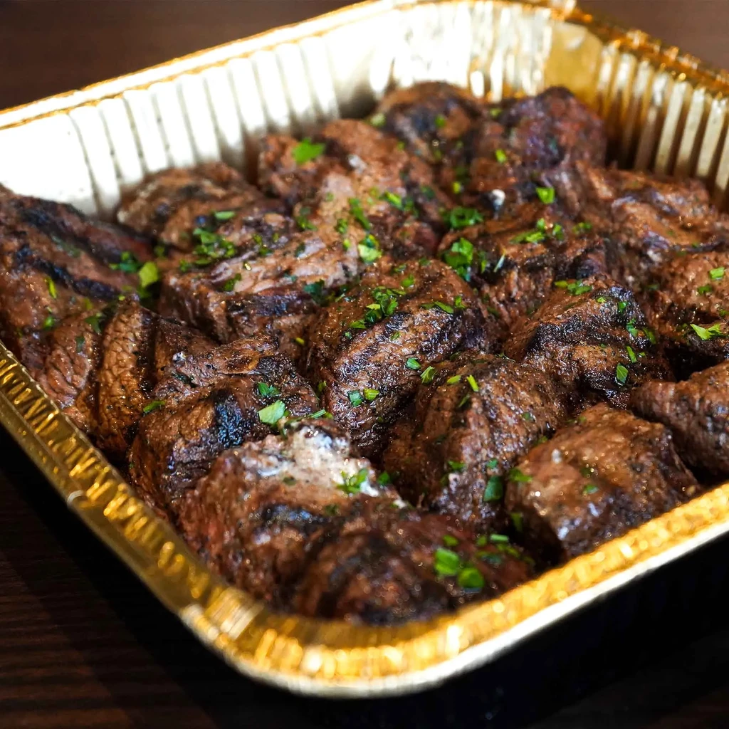 Grilled meat pieces in a foil tray, garnished with green herbs.