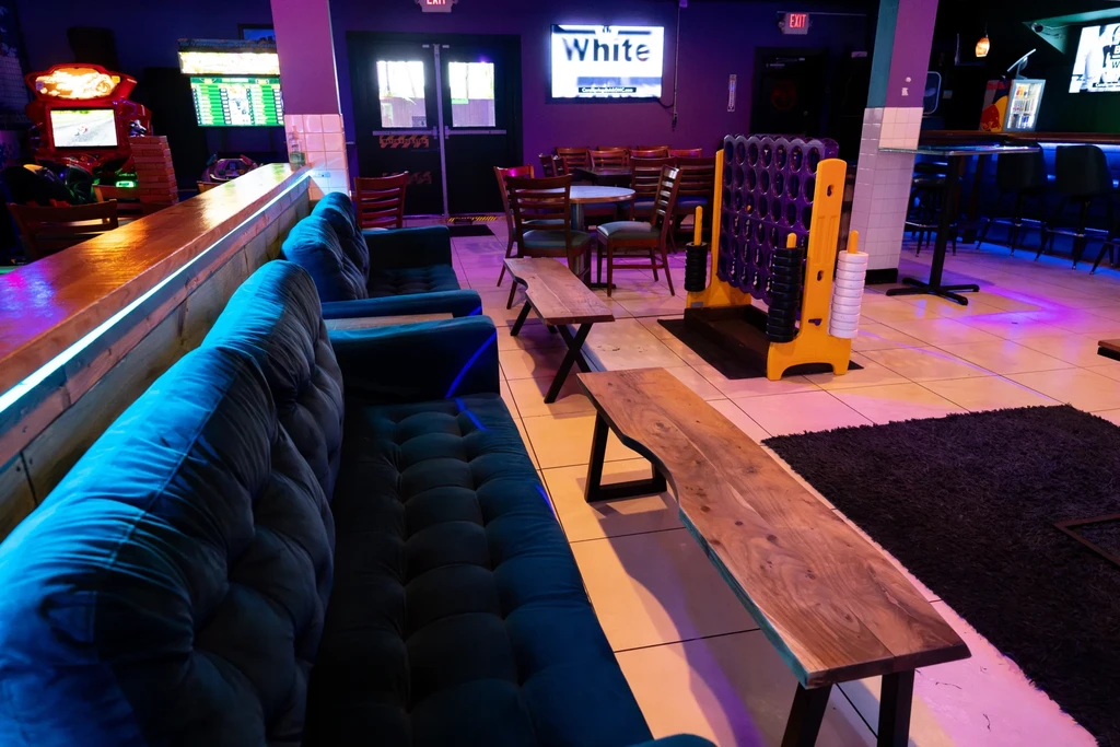 Vibrant modern bar with teal sofas, arcade games, and giant Connect Four.