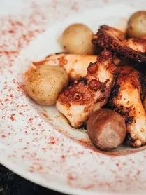 Grilled octopus and roasted potatoes with paprika on a white plate.
