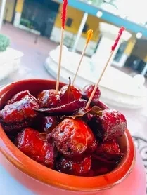 Glossy red food in ceramic bowl with decorative toothpicks and chili.