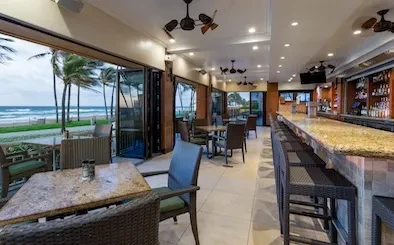 Upscale beachfront restaurant interior with ocean view through open doors.