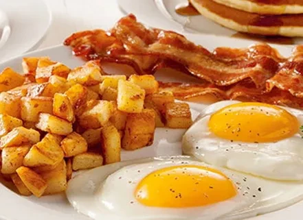 Two sunny-side-up eggs, home fries, bacon, and pancakes on a plate.