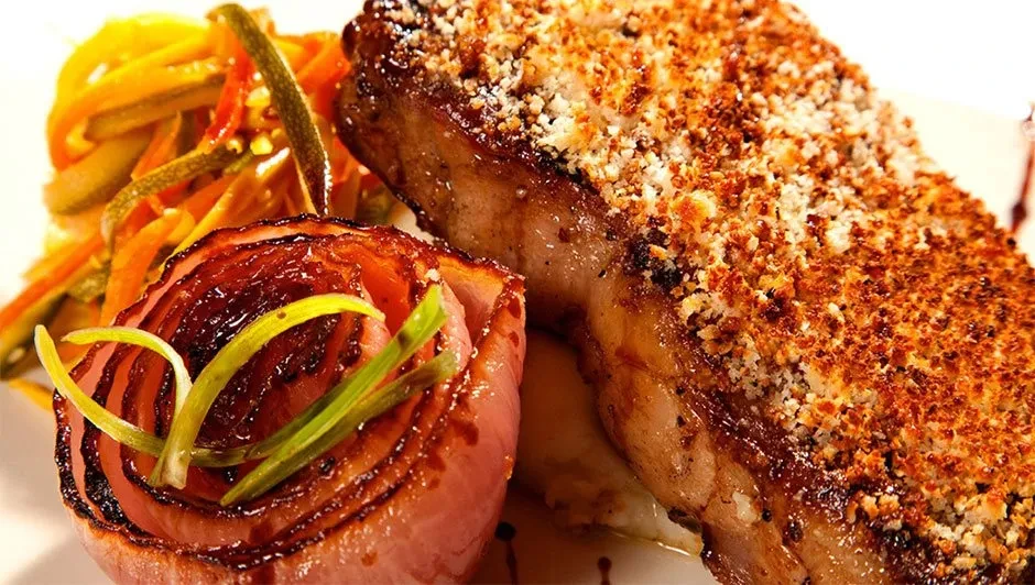 Crusted meat, caramelized red onion, and julienned vegetables on a plate.