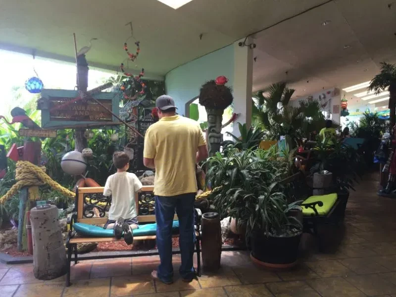 Restaurant interior with tropical plants, nautical decor, and two people.