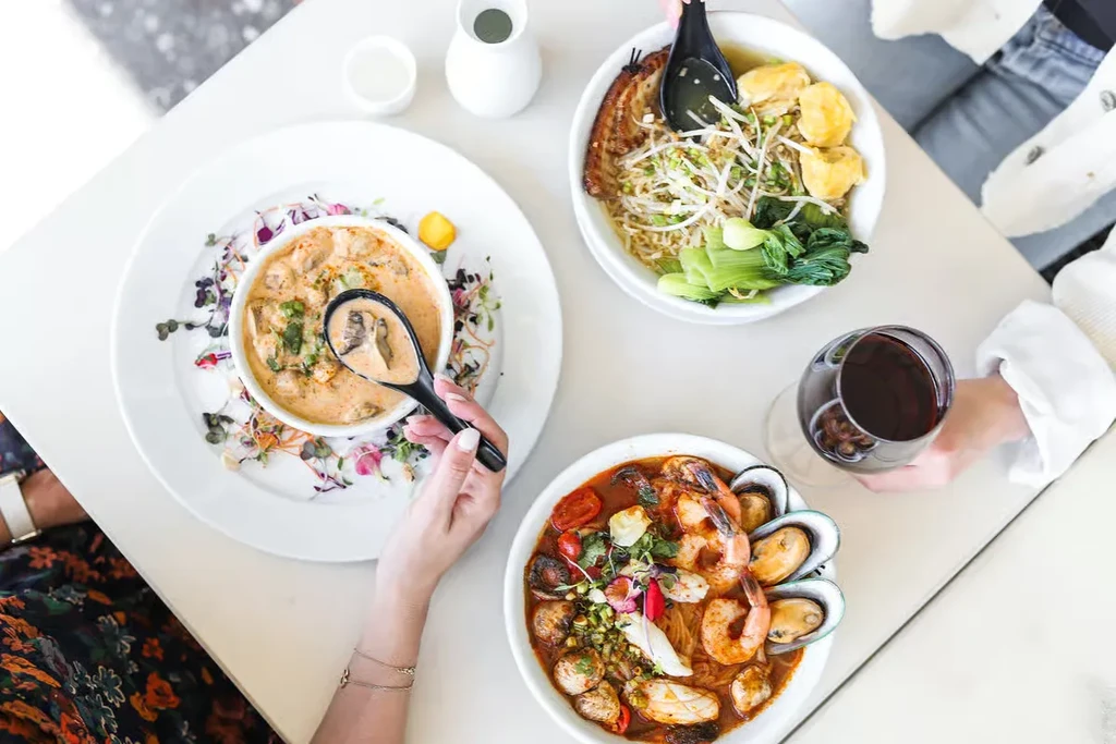 Three diverse food bowls, red wine, and hands sharing a meal.
