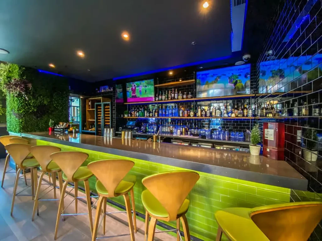 Modern bar with lime-green stools, LED lights, and living wall.