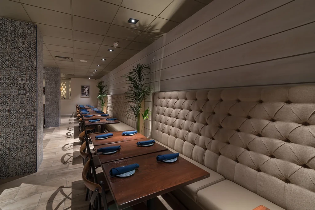 Empty modern restaurant with tan booths, patterned tiles, and potted plants.
