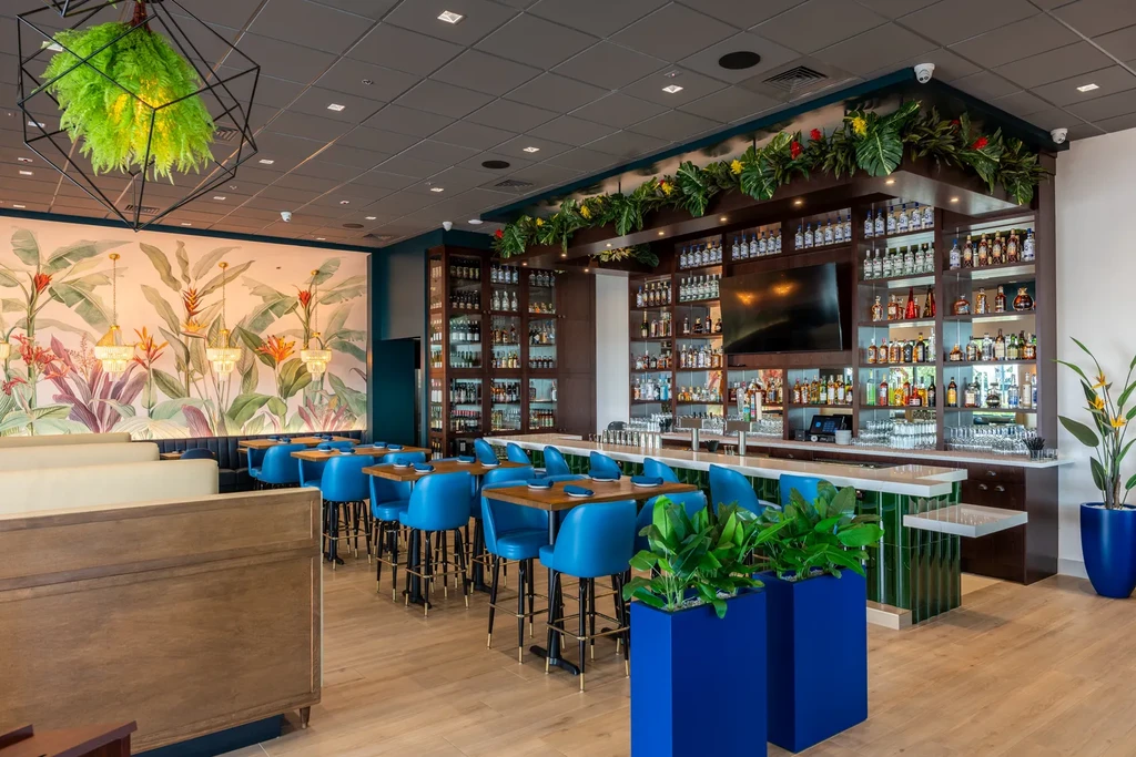 Vibrant tropical restaurant interior with blue chairs, mural, and well-stocked bar.