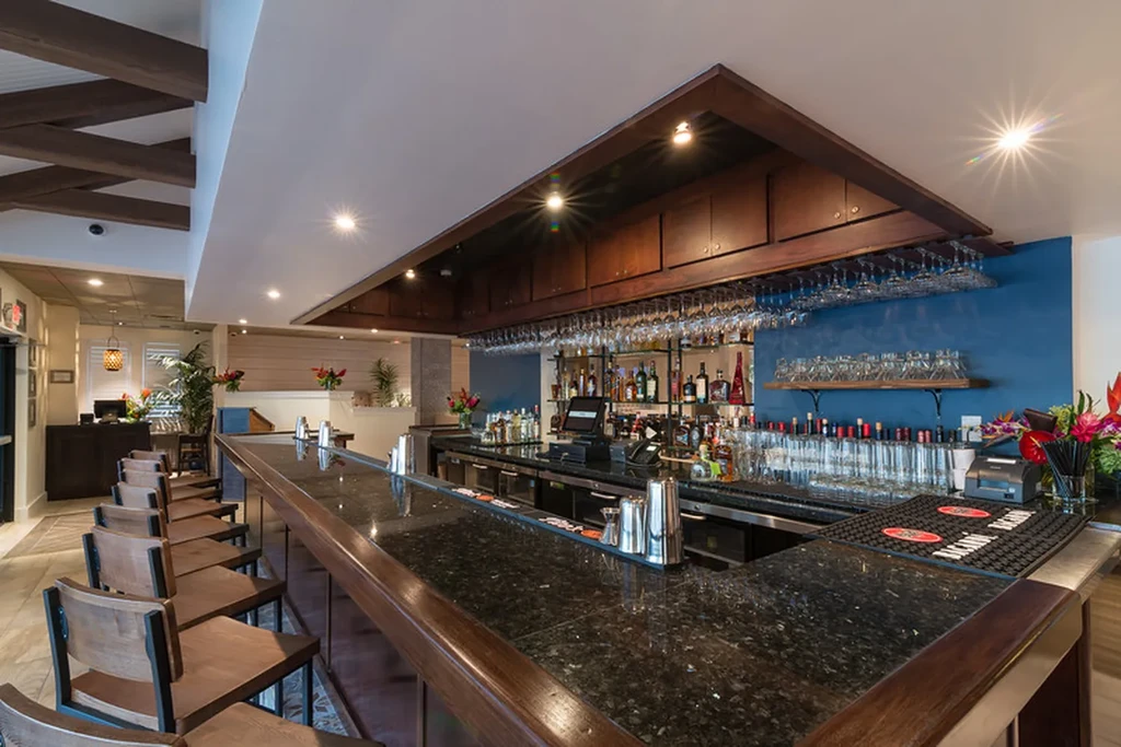 Empty restaurant bar with dark counter, stools, stocked back, blue wall.