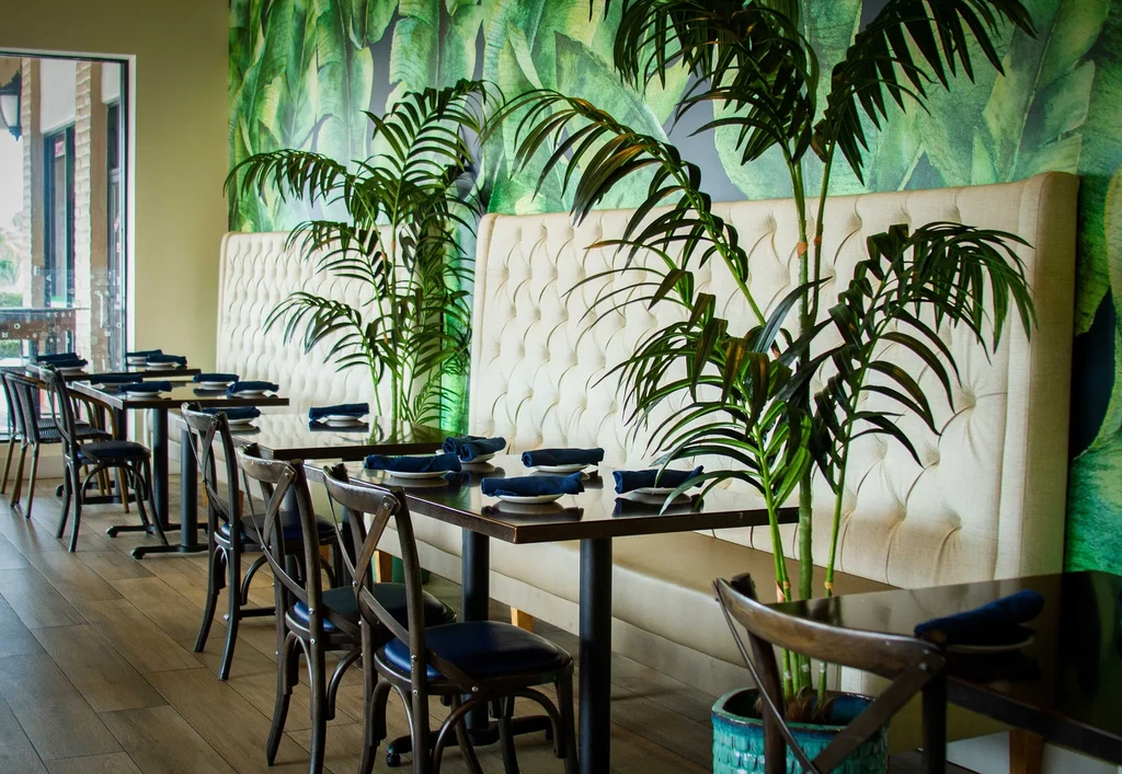 Empty restaurant interior with tropical leaf wallpaper and booth seating.