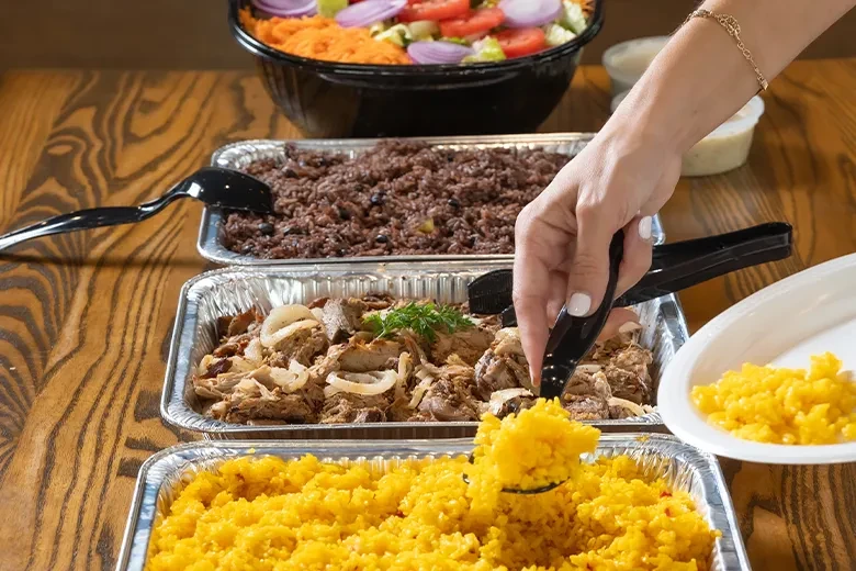 Hand serving yellow rice from a buffet with salad and meat dishes.