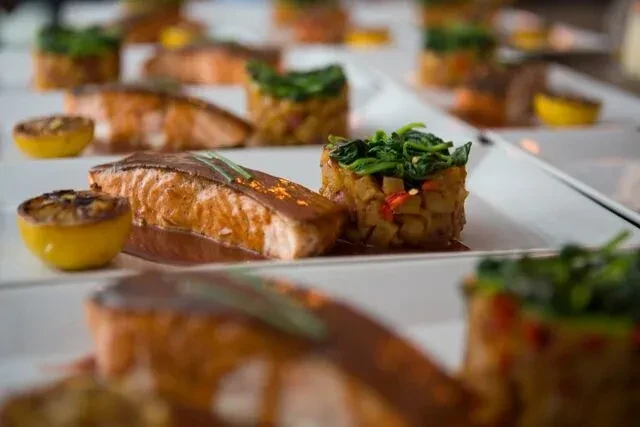 Plated salmon, vegetable medley, spinach, and grilled lemon in rows.