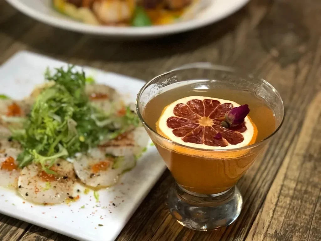 Amber cocktail, blood orange, rosebud, scallop carpaccio, wood table.