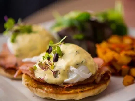 Two Eggs Benedict with microgreens, salad, and seasoned potato cubes.