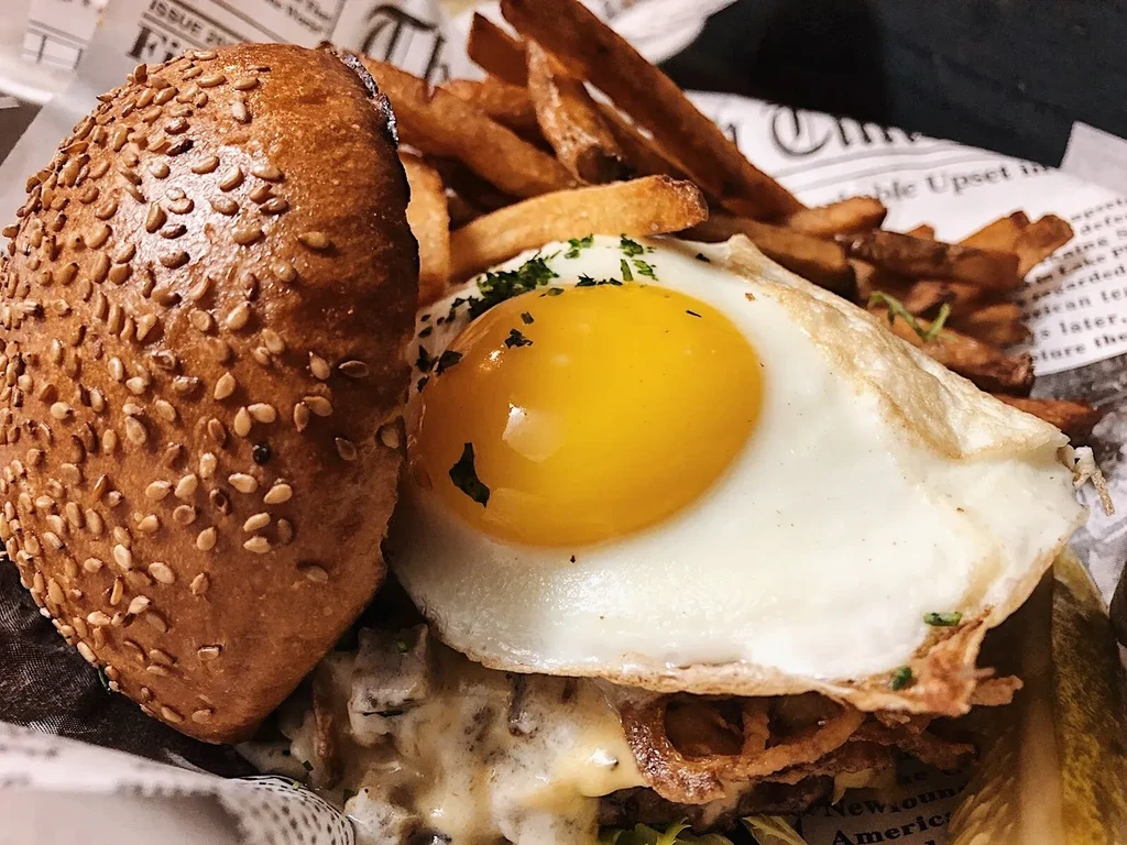 Burger with fried egg, melted cheese, crispy onions, and fries.