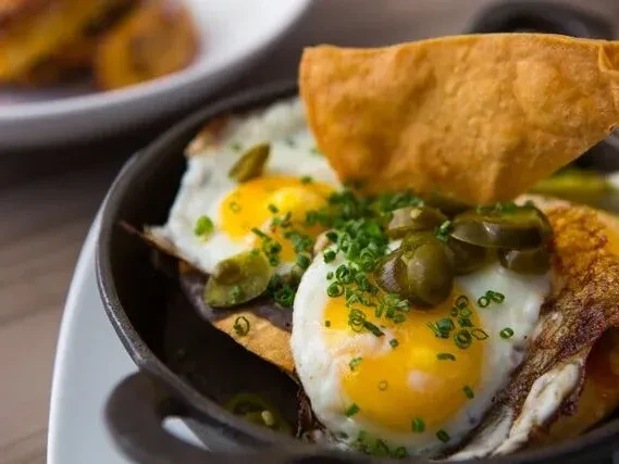 Skillet with two fried eggs, chives, jalapeños, and tortilla chips.