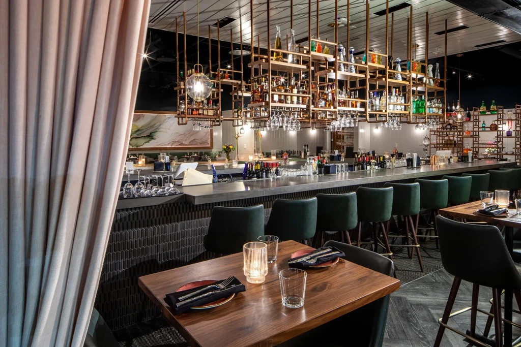 Sleek modern restaurant bar area with golden shelving and set tables.