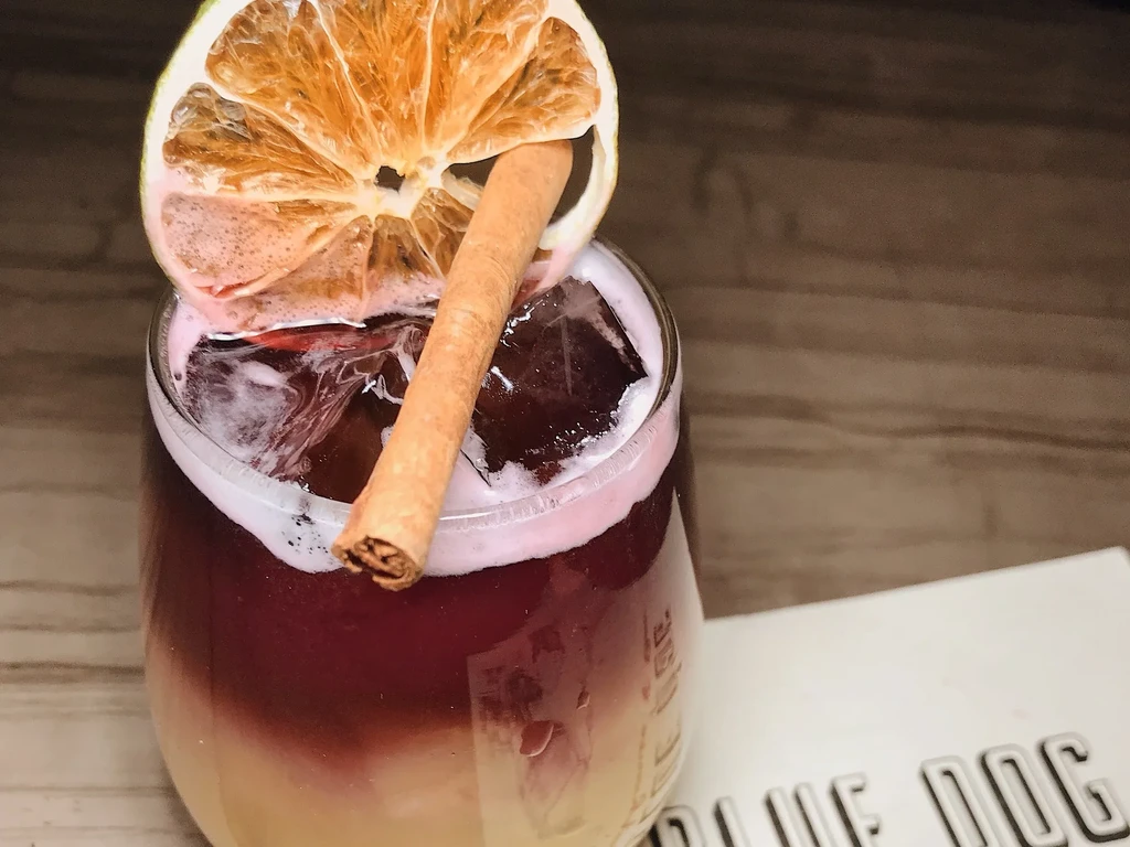 Layered cocktail with ice, orange slice, and cinnamon stick.