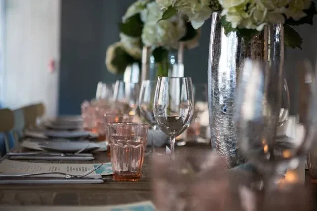 Dining table set with clear and pink glasses and white flowers.