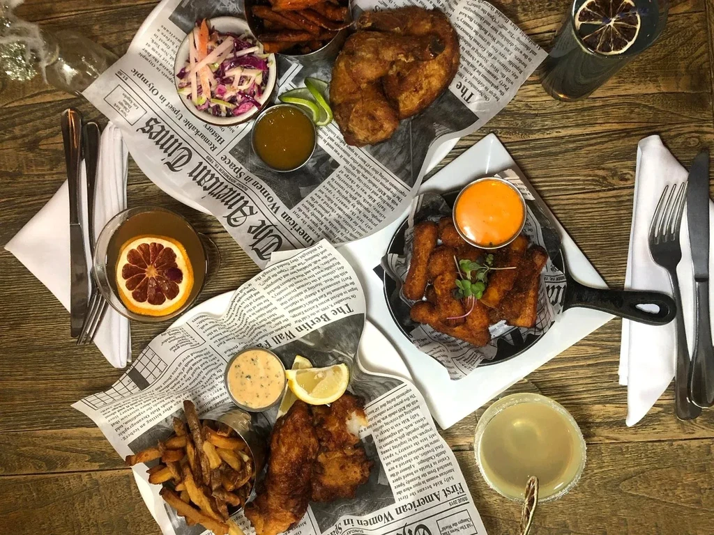 Rustic table with flat lay of fried food, fries, coleslaw, and drinks.