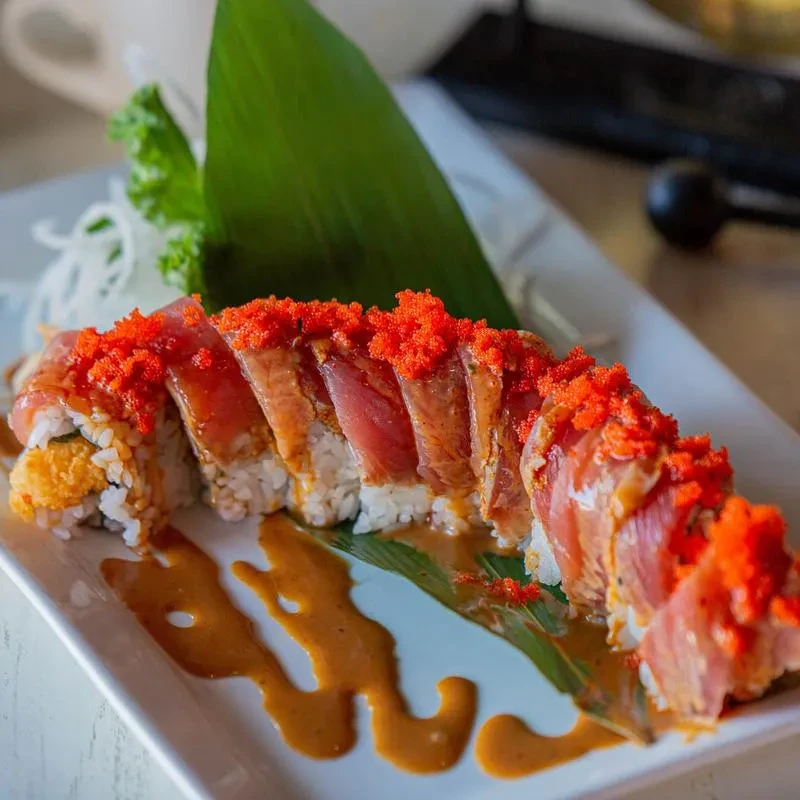 Sliced tuna sushi roll with tobiko, fried filling, sauce, and garnishes.