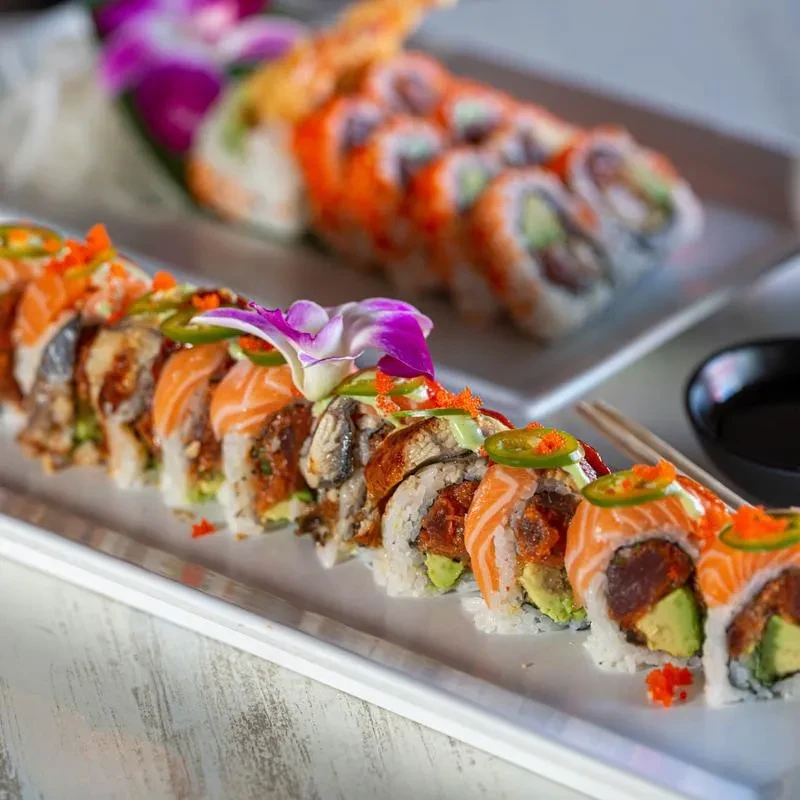 Artfully arranged sushi rolls with salmon, eel, avocado, roe, and orchid.