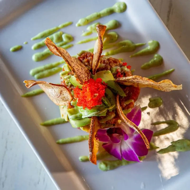 Stacked tartare with avocado, red roe, chips, green sauce, and orchid.