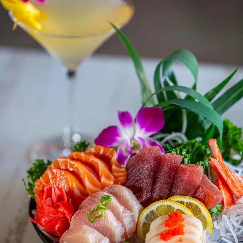 Vibrant sushi and sashimi platter featuring raw fish and a blurred cocktail.