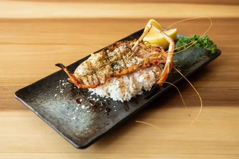 Grilled prawn halved on white rice, lemon and green garnish.