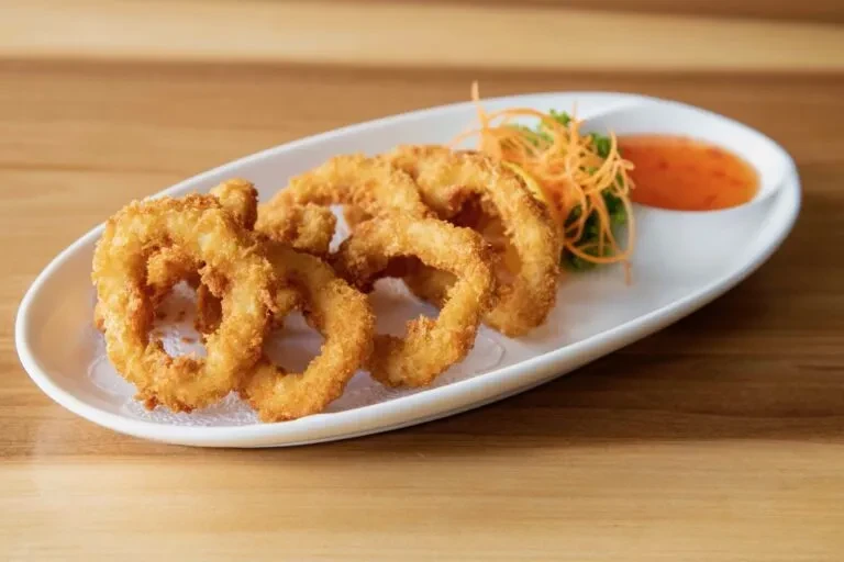 Fried calamari/onion rings on platter with orange sauce and garnish.
