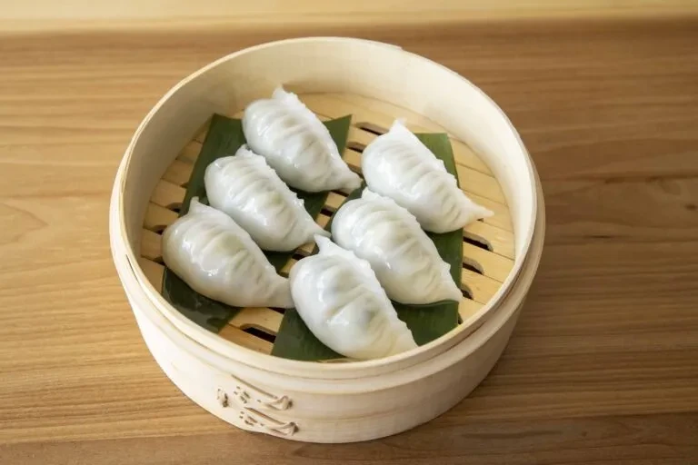 Seven translucent dumplings on banana leaf in a bamboo steamer.
