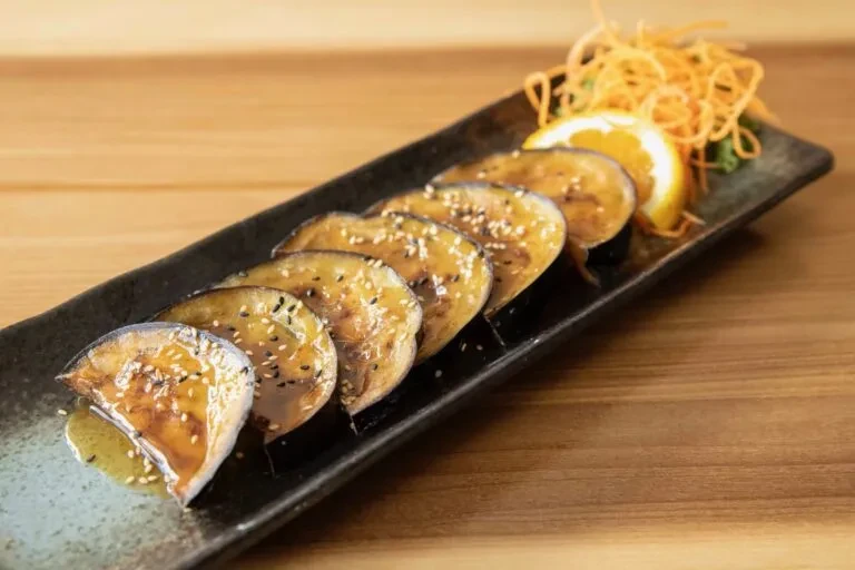 Grilled eggplant with glossy sauce, sesame seeds, and orange garnish.