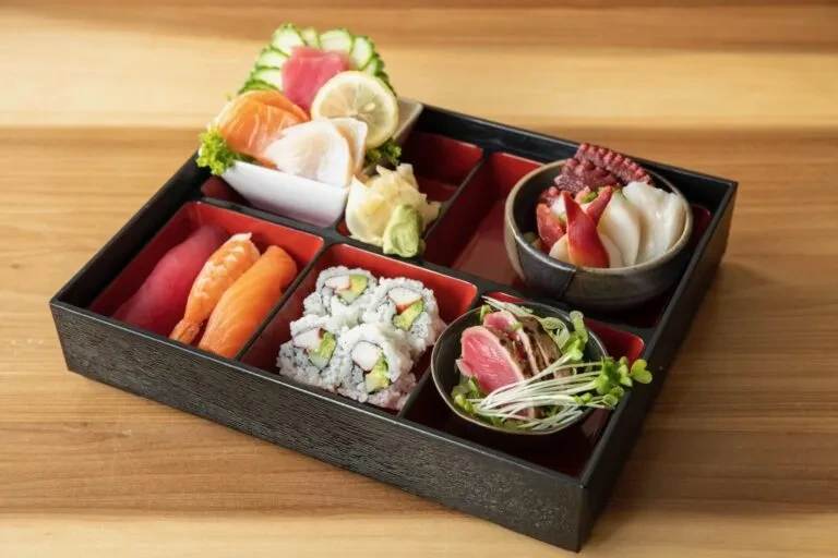 Japanese bento box with sashimi, sushi, and seafood salads on wood.