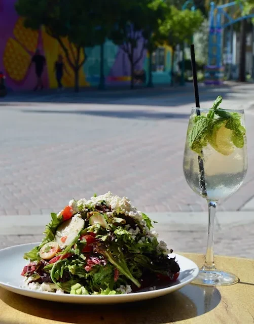 Fresh green salad with feta, tomatoes, and mint drink on outdoor table.