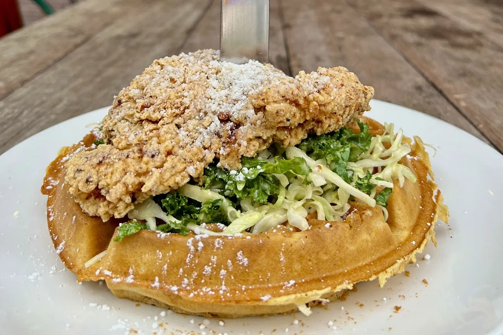 Fried chicken and waffle dish with coleslaw, powdered sugar, and a knife.