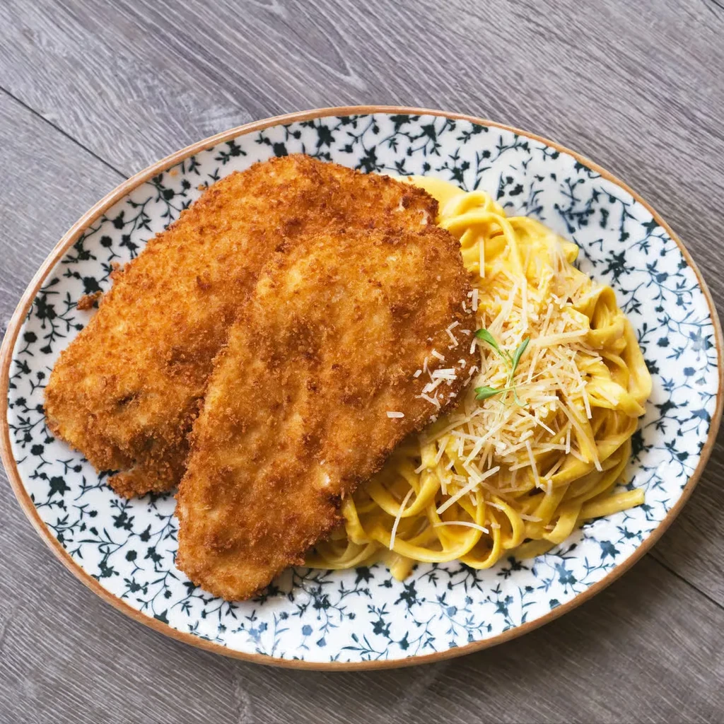 Two breaded cutlets, pasta with cheese, and herb on a patterned plate.