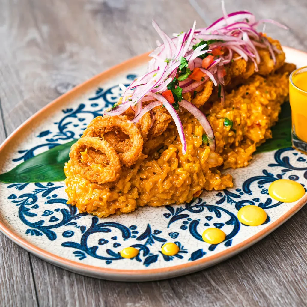 Dish of orange rice with fried calamari, red onions, and green herbs.