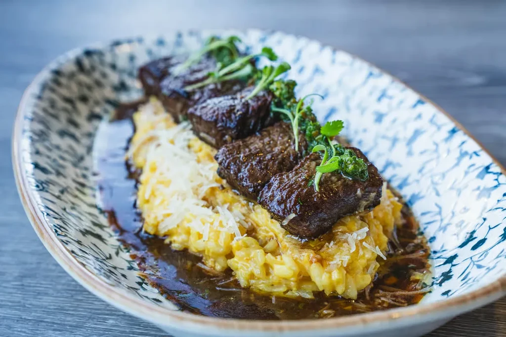 Seared steak with creamy risotto, topped with cheese and green herbs.