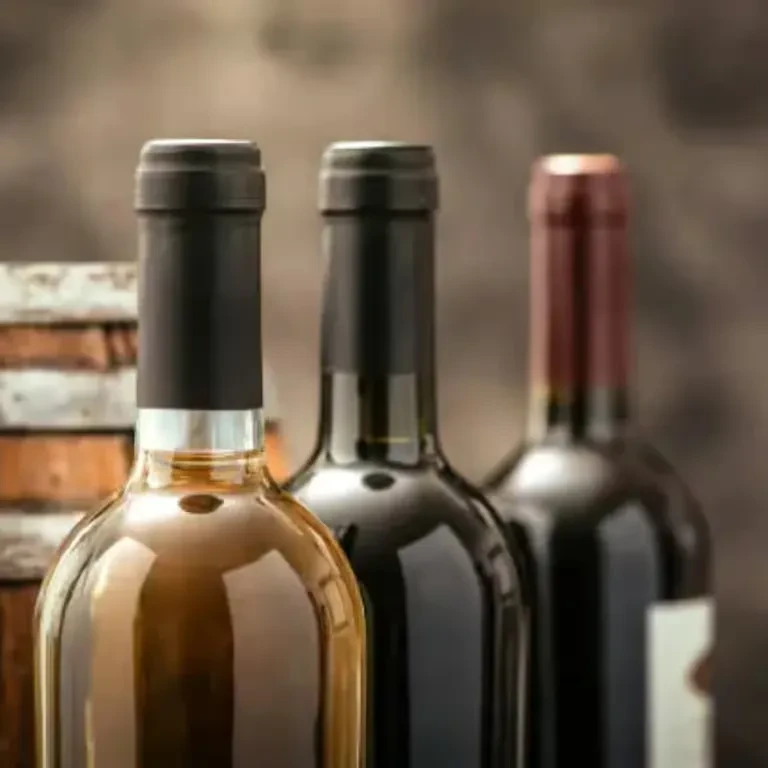 Three wine bottles: one white, two red, with a rustic background.