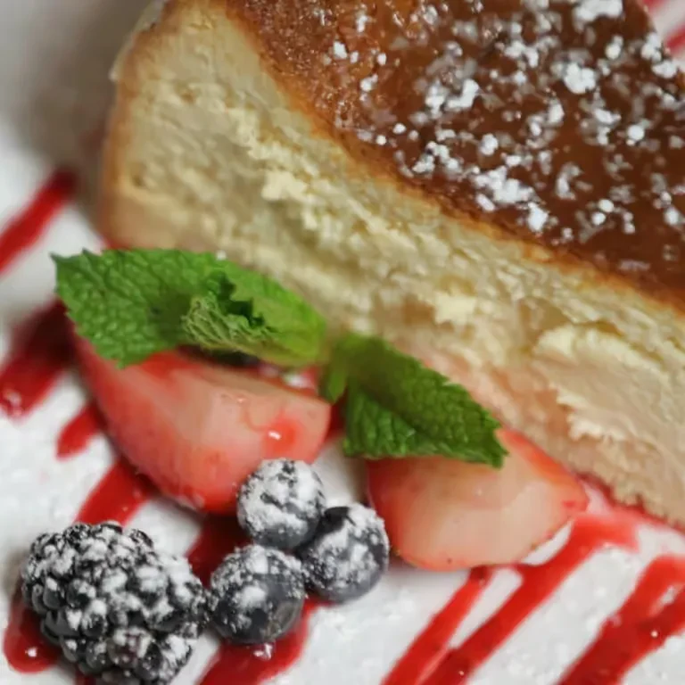 Cheesecake slice with berries, mint, powdered sugar, and berry sauce.
