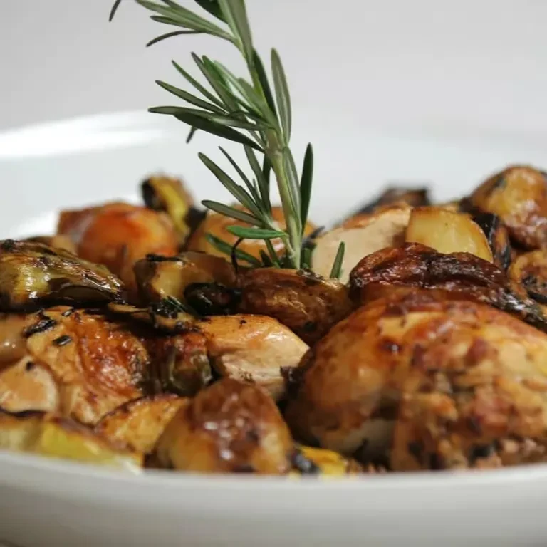 Golden roasted chicken and vegetables with rosemary in a white bowl.