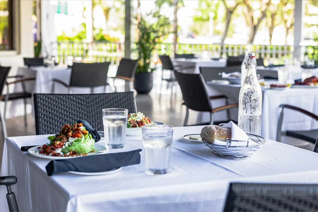 Outdoor restaurant table with salad, bread, chilled water, and green trees.