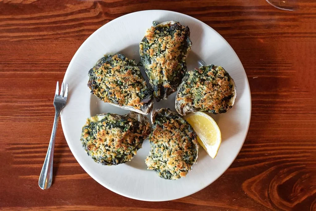 Five baked oysters with green herbs, golden breadcrumbs, lemon wedge.