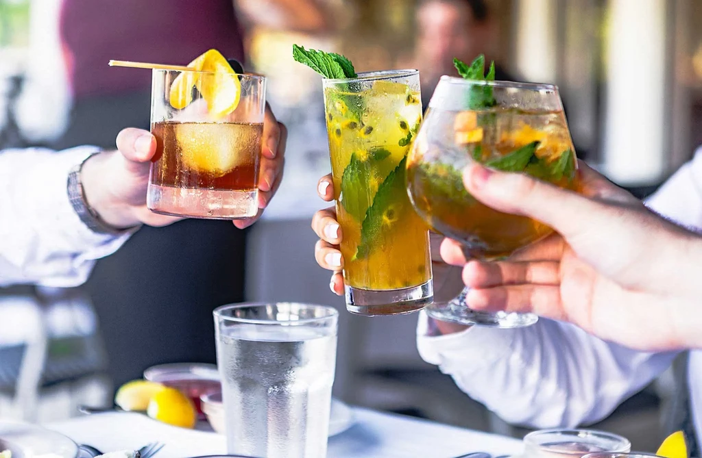 People toasting with three different vibrant cocktails.