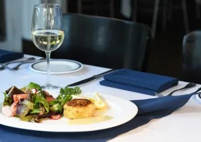 Restaurant table with a crab cake, salad, lemon, and white wine.