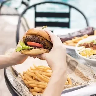 Hands holding a burger with cheese, tomato, lettuce, and golden fries.