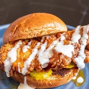 Golden-brown fried chicken sandwich with creamy sauce, pickles, and toasted bun.