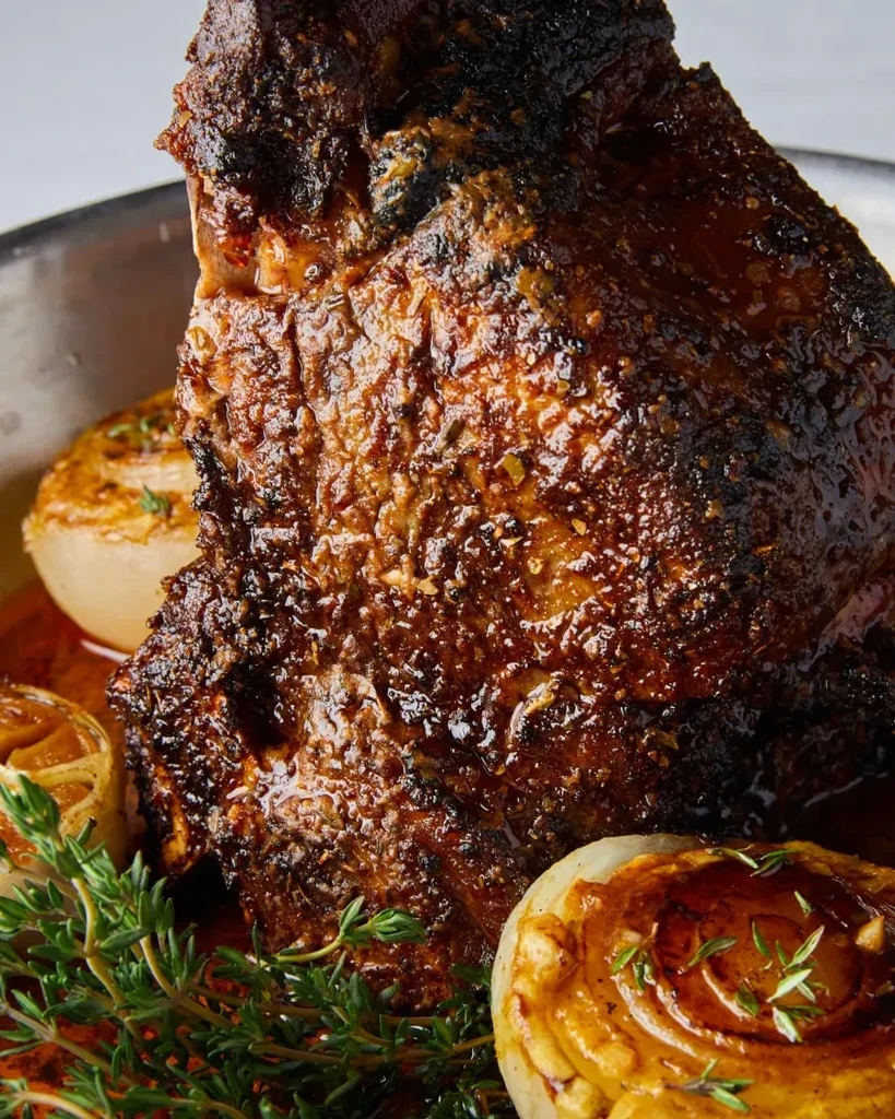 Glistening roasted meat with caramelized crust, roasted onions, and fresh thyme.